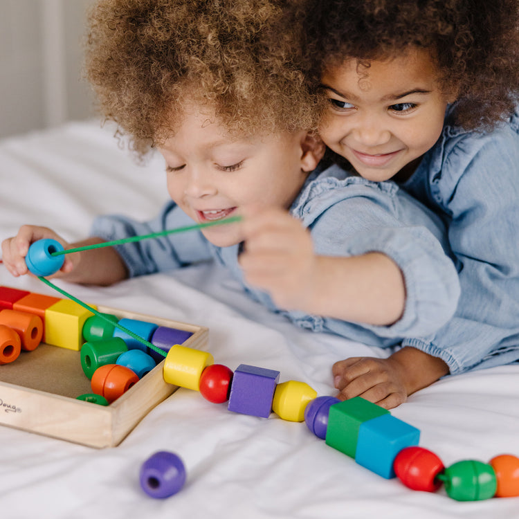 A kid playing with The Melissa & Doug Primary Lacing Beads - Educational Toy With 30 Wooden Beads and 2 Laces