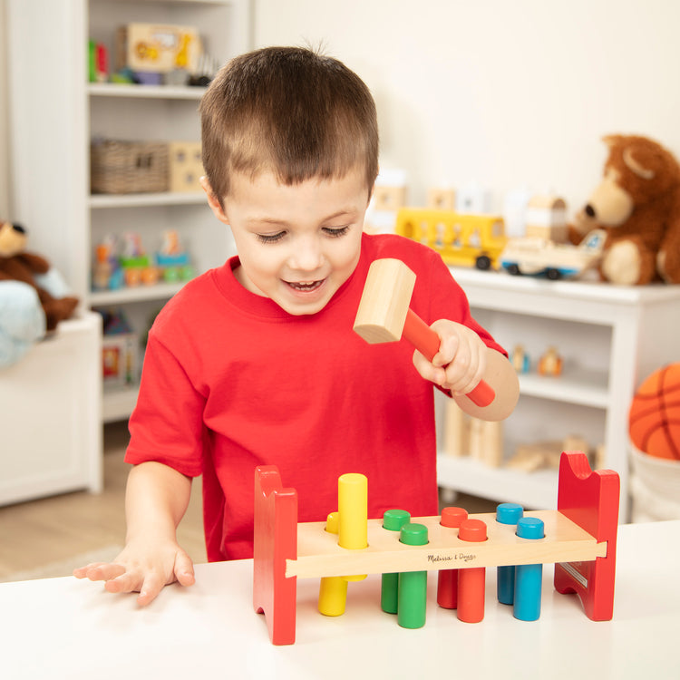 A kid playing with The Melissa & Doug Deluxe Wooden Pound-A-Peg Toy With Hammer