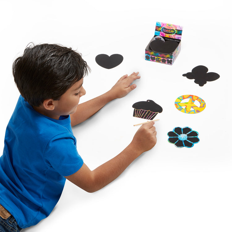 A child on white background with The Melissa & Doug Scratch Art® Box of 125 Friendship-Themed Shaped Notes in Desktop Dispenser (Approx. 3.5” x 3.5” Each Note)