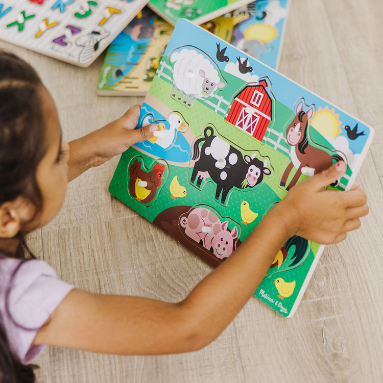 A kid playing with The Melissa & Doug Wooden Peg Puzzle 6-Pack – Numbers, Letters, 3 Animals, Vehicles