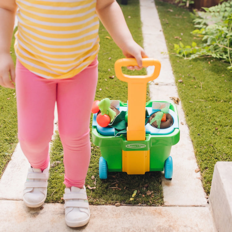 A kid playing with The Melissa & Doug Let’s Explore Vegetable Gardening Play Set with Rolling Cart (31 Pieces)