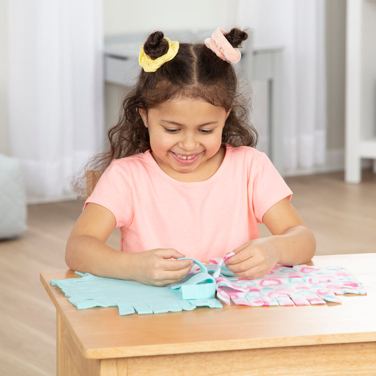 A kid playing with The Melissa & Doug Created by Me! Heart Fleece Blanket No-Sew Craft Kit (40 squares, 3.5 feet x 5 feet)