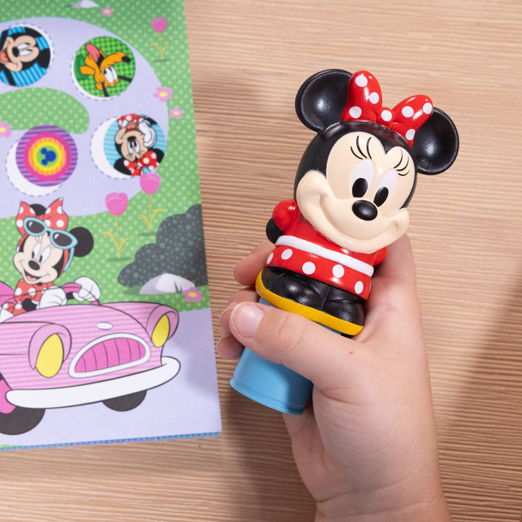 A kid playing with The Melissa & Doug Sticker WOW!™ 24-Page Activity Pad and Sticker Stamper, 300 Stickers, Arts and Crafts Fidget Toy Collectible Character – Disney Minnie Mouse