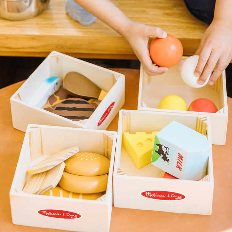 A kid playing with The Melissa & Doug Food Groups - 21 Wooden Pieces and 4 Crates, Multi