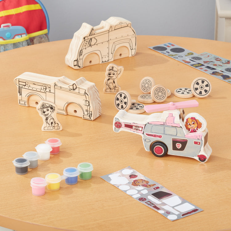 A playroom scene with The Melissa & Doug PAW Patrol Wooden Vehicles Craft Kit - 3 Decorate Your Own Vehicles, 3 Play Figures