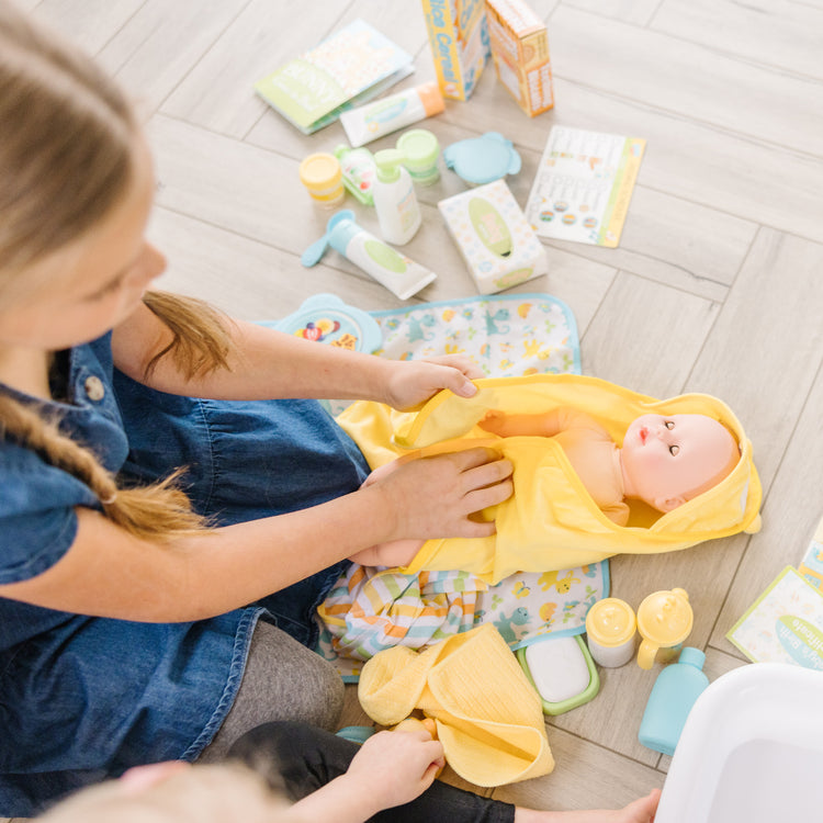 A kid playing with The Melissa & Doug Mine to Love Deluxe Baby Care Play Set (48 Pieces – Doll + Accessories to Feed, Bathe, Change, and Cuddle)