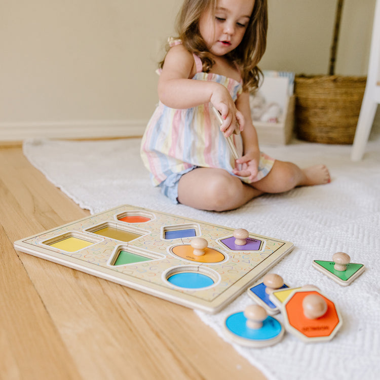 A kid playing with The Melissa & Doug Deluxe Jumbo Knob Wooden Puzzle - Geometric Shapes (8 pcs)