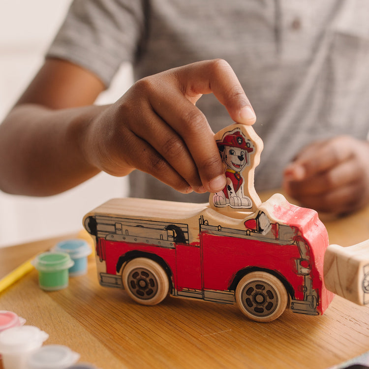 A kid playing with The Melissa & Doug PAW Patrol Wooden Vehicles Craft Kit - 3 Decorate Your Own Vehicles, 3 Play Figures