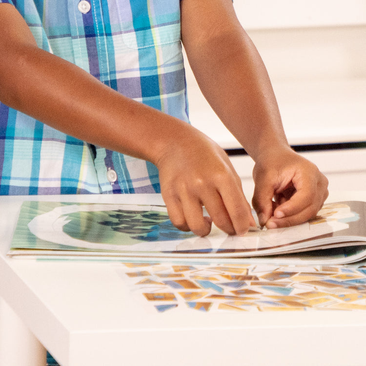 A kid playing with The Melissa & Doug Mosaic Sticker Pad Safari Animals (12 Color Scenes to Complete with 850+ Stickers)