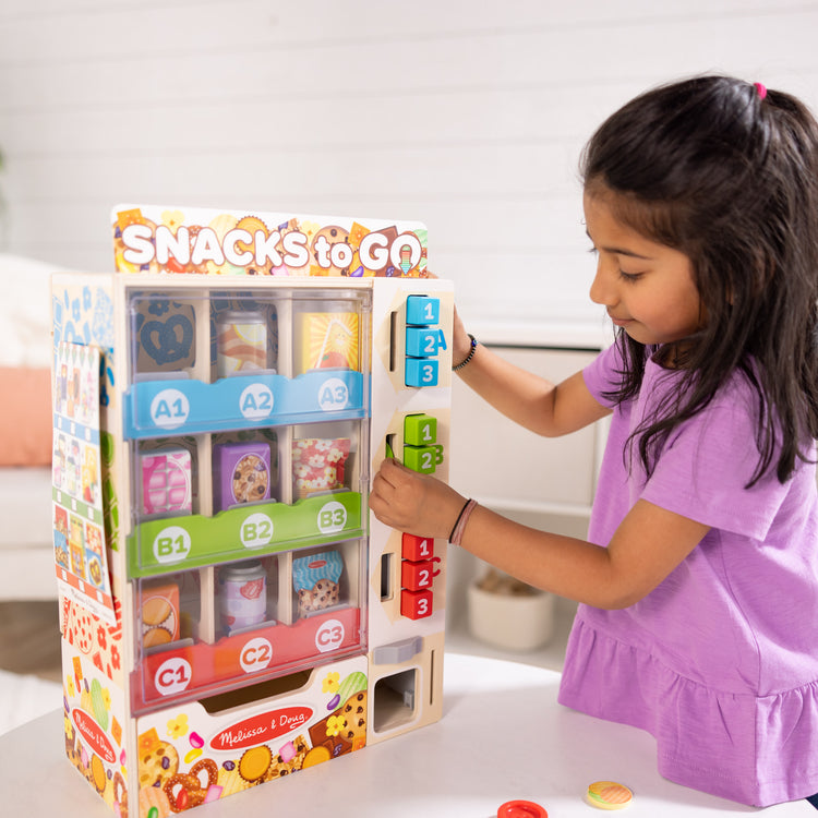 A kid playing with The Melissa & Doug Sort, Stock, Select Wooden Vending Machine Play Set, Wooden Toy Play Food For Boys and For Girls 3+