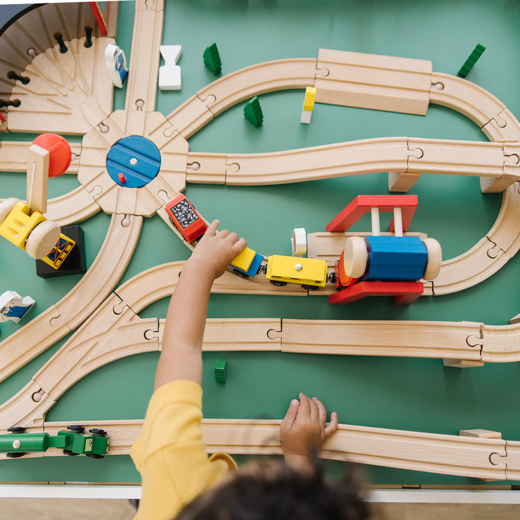A kid playing with The Melissa & Doug Deluxe Wooden Railway Train Set (130+ pcs)