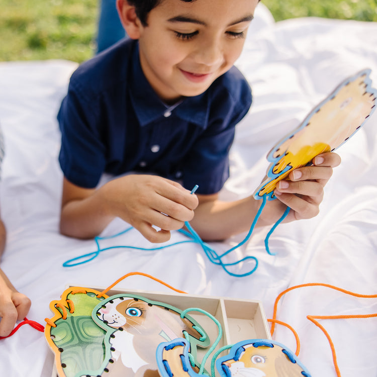 A kid playing with The Melissa & Doug Lace and Trace Activity Set: Pets - 5 Wooden Panels and 5 Matching Laces