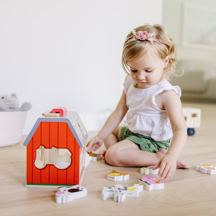 A kid playing with The Melissa & Doug Wooden Take-Along Sorting Barn Toy with Flip-Up Roof and Handle 10 Wooden Farm Play Pieces