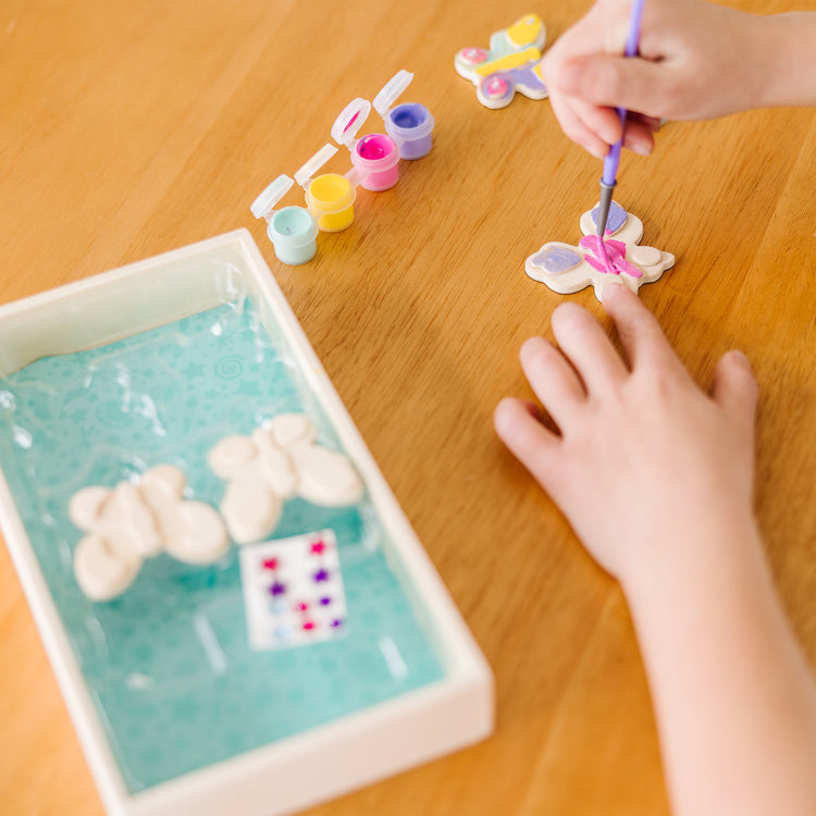 A kid playing with The Melissa & Doug Created by Me! Wooden Butterfly Magnets Craft Kit (4 Designs, 4 Paints, Stickers, Glitter Glue)