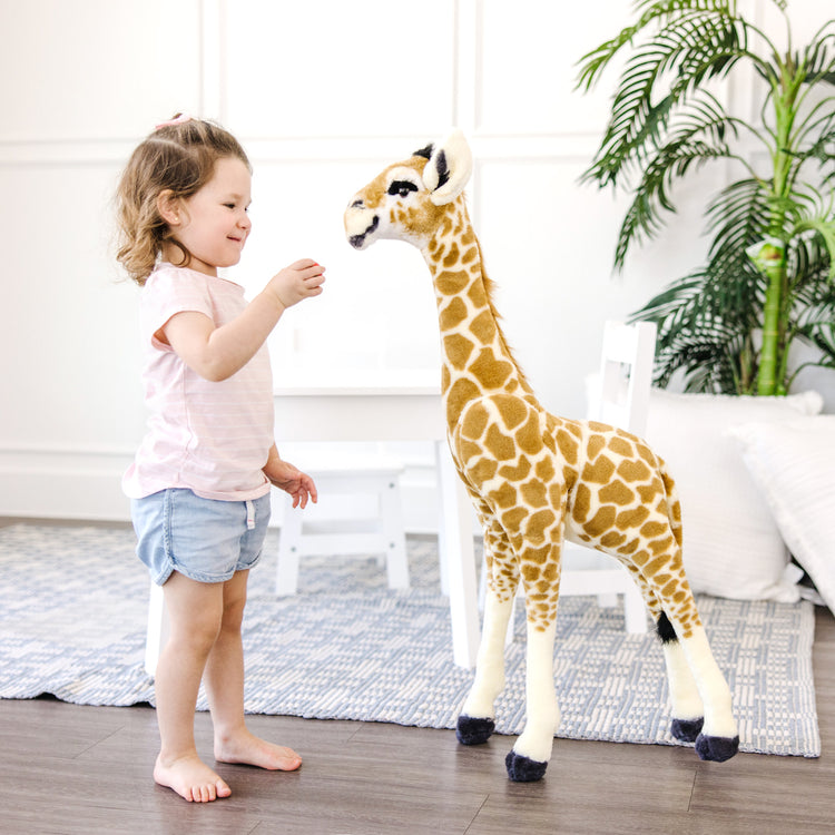 A kid playing with The Melissa & Doug Lifelike Plush Standing Baby Giraffe Stuffed Animal – 3 Feet Tall