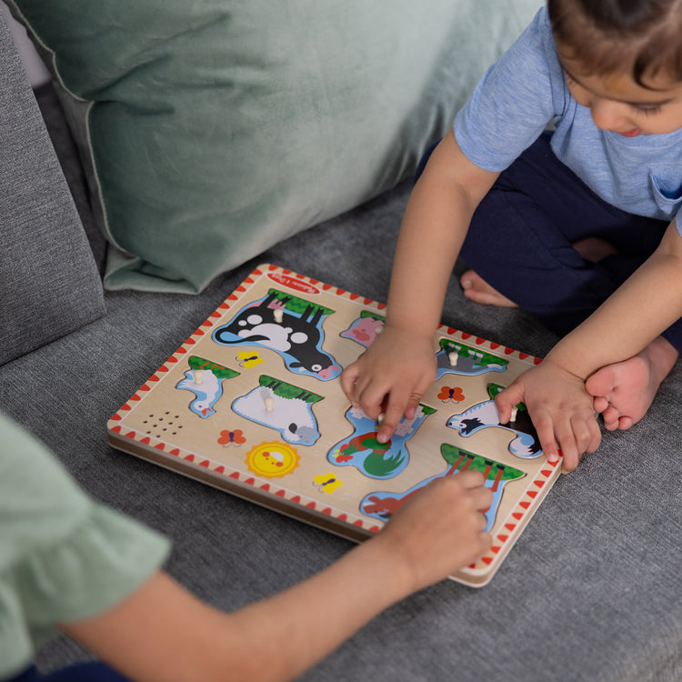 A kid playing with The Melissa & Doug Wooden Sound Puzzle 2-Pack for Toddler and Preschool Boys and Girls – Farm Animals, Vehicles