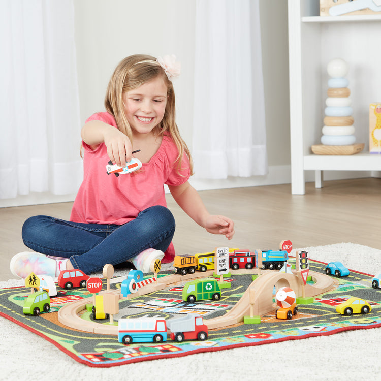 A kid playing with The Melissa & Doug Deluxe Multi-Vehicle Activity Rug (39.5" x 36.5") - 19 Vehicles, 12 Wooden Signs, Train Tracks