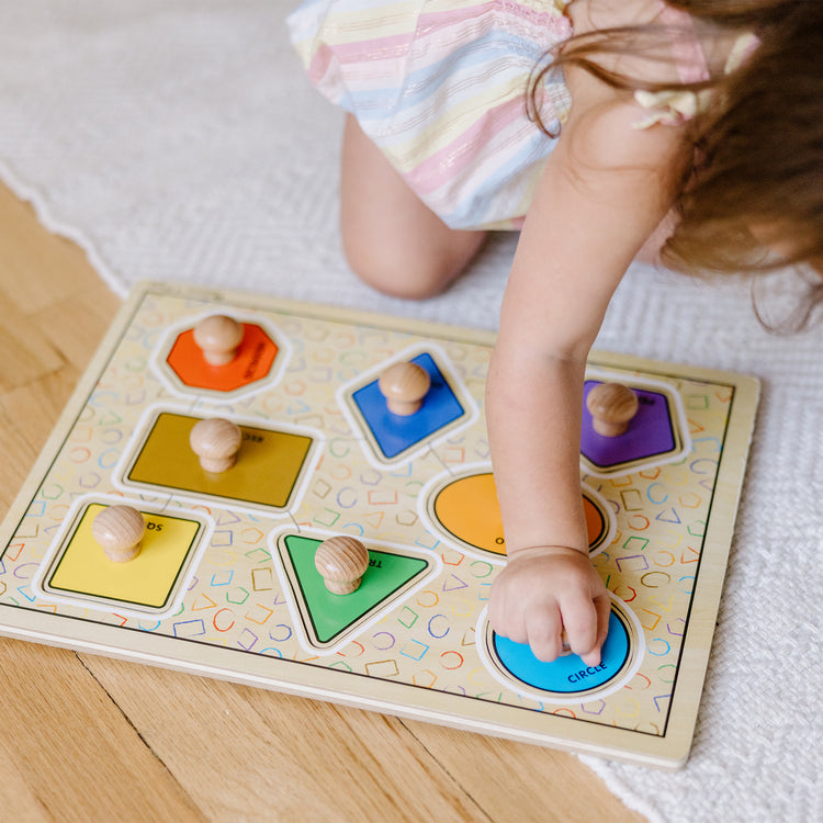 A kid playing with The Melissa & Doug Deluxe Jumbo Knob Wooden Puzzle - Geometric Shapes (8 pcs)