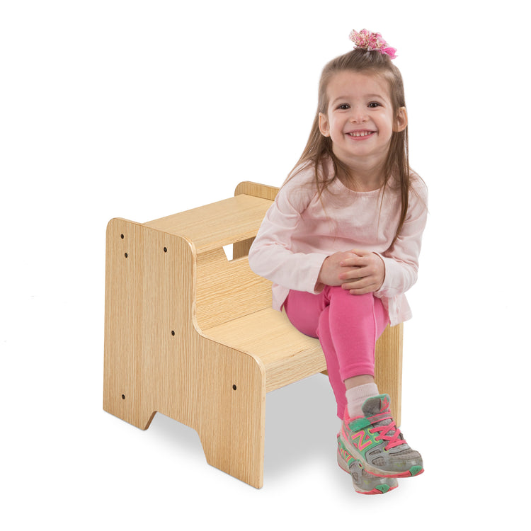 A child on white background with The Melissa & Doug Kids Wooden Step Stool - Light Natural Finish