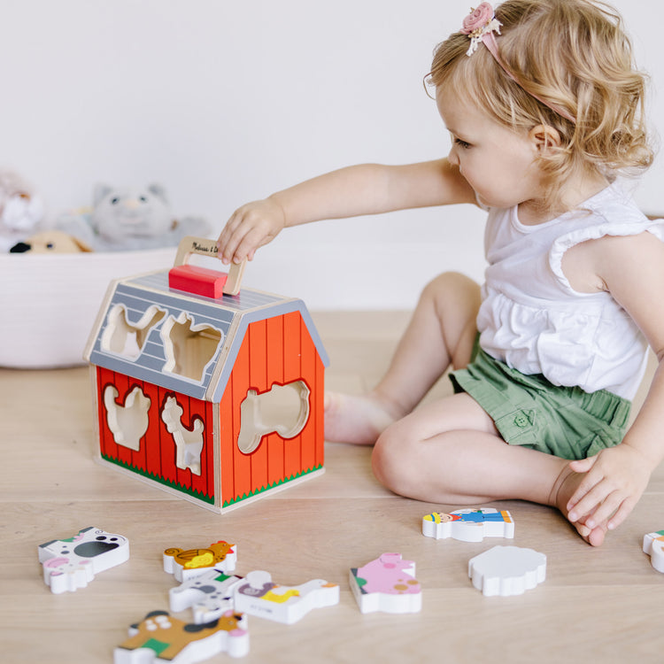 A kid playing with The Melissa & Doug Wooden Take-Along Sorting Barn Toy with Flip-Up Roof and Handle 10 Wooden Farm Play Pieces