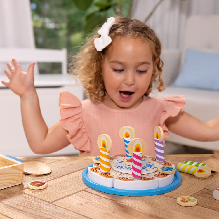 A kid playing with The Melissa & Doug Birthday Party Cake - Wooden Play Food With Mix-n-Match Toppings and 7 Candles