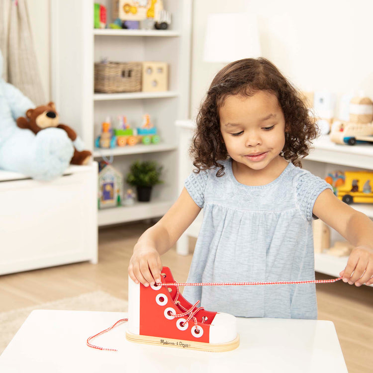 A kid playing with The Melissa & Doug Deluxe Wood Lacing Sneaker - Learn to Tie a Shoe Educational Toy
