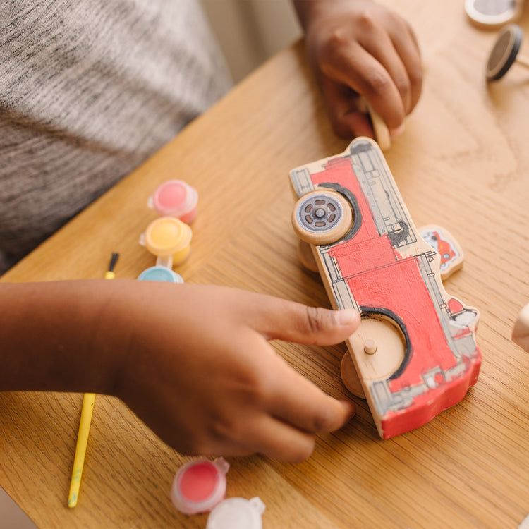 A kid playing with The Melissa & Doug PAW Patrol Wooden Vehicles Craft Kit - 3 Decorate Your Own Vehicles, 3 Play Figures