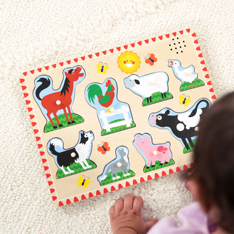 A kid playing with The Melissa & Doug Farm Animals Sound Puzzle - Wooden Peg Puzzle With Sound Effects (8 pcs)