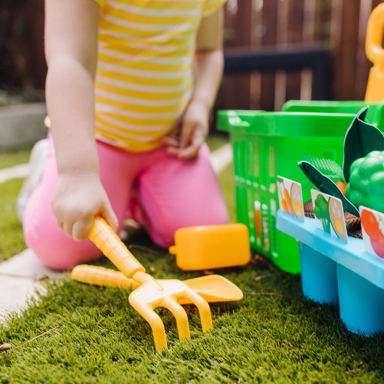 A kid playing with The Melissa & Doug Let’s Explore Vegetable Gardening Play Set with Rolling Cart (31 Pieces)