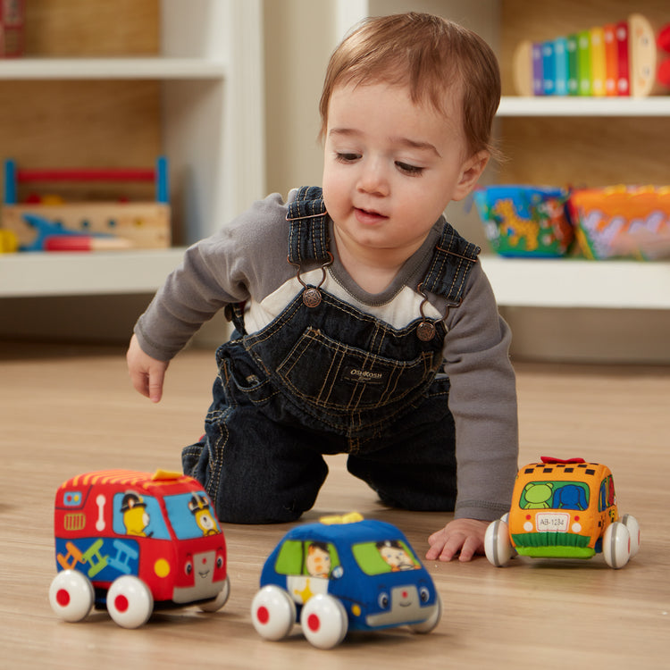 A kid playing with The Melissa & Doug K's Kids Pull-Back Vehicle Set - Soft Baby Toy Set With 4 Cars and Trucks and Carrying Case