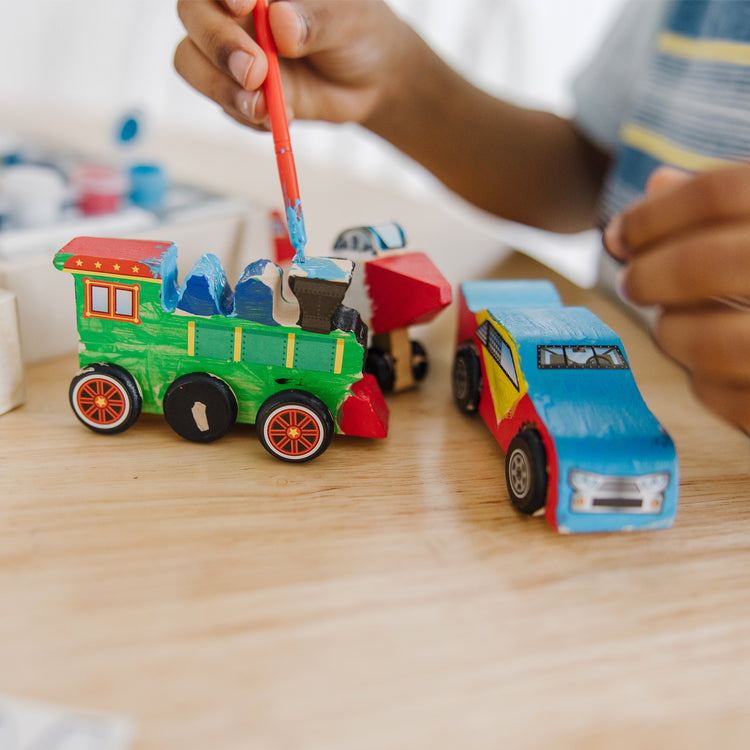 A kid playing with The Melissa & Doug Decorate-Your-Own Wooden Craft Kits 3-Pack - Plane, Train, and Race Car