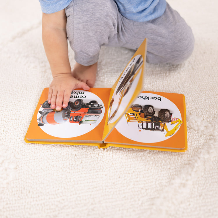 A kid playing with The Melissa & Doug Children’s Book – Poke-a-Dot: Construction Vehicles (Board Book with Buttons to Pop)