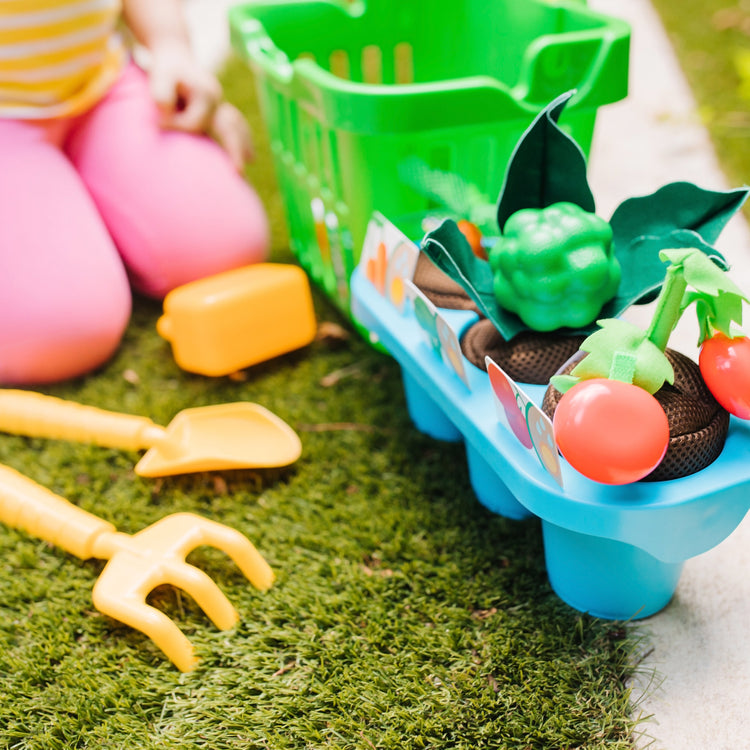 A kid playing with The Melissa & Doug Let’s Explore Vegetable Gardening Play Set with Rolling Cart (31 Pieces)